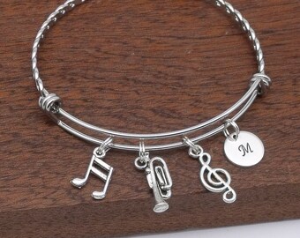 May include: Silver expandable bracelet with charms including a treble clef, musical note, trumpet, and a charm with the letter "M".