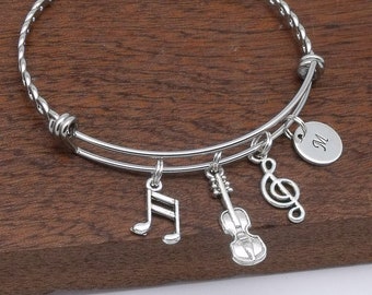 May include: Silver charm bracelet with a music note, violin, treble clef, and initial charm. The bracelet is made of twisted metal and has a spring clasp.