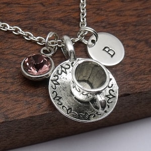 May include: Silver necklace with a charm of a teacup and saucer, a pink crystal, and a round charm with the letter "B" engraved on it.