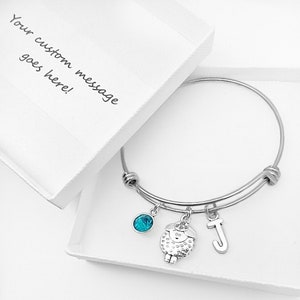 May include: A silver expandable bangle bracelet with a turquoise charm, a silver charm of a sheep, and a silver charm with the letter J.