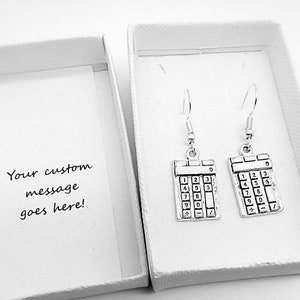 May include: A pair of silver calculator earrings in a white gift box. The earrings are shaped like a calculator with the numbers 0-9 and the symbols +,-,*, and /. The box has a white card inside with the text "Your custom message goes here!"