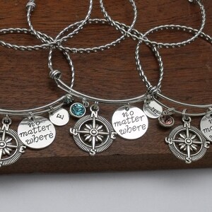 May include: Three silver charm bracelets with compass charms and "no matter where" engraved charms. Each bracelet has a small initial charm and a crystal charm.