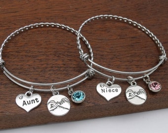 May include: Two silver charm bracelets with the words "Aunt" and "Niece" on heart-shaped charms. Each bracelet also has a charm with two hands holding pinkies together and a small crystal charm.