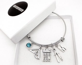 May include: A silver charm bracelet with a blue crystal charm, a protractor, a calculator, a compass, and a letter 'M' charm. The bracelet is in a white box.