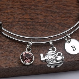 May include: A silver expandable bangle bracelet with three charms: a pink crystal, a teapot with a cup, and a silver disc with the letter "B" engraved on it.