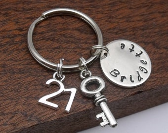 May include: Silver keychain with a key charm, a charm with the number 21, and a round charm with the word "Bridge" engraved on it.