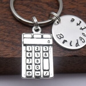 May include: Silver calculator keychain with a silver charm that says "Bridge the gap".