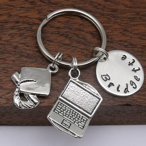 May include: Silver keyring with a graduation cap, laptop, and a personalised tag that says "Bridgetta".
