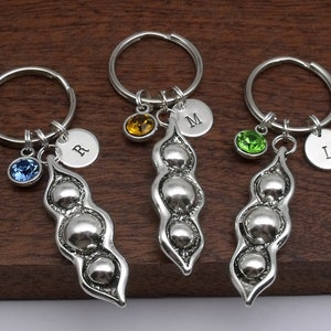 May include: Three silver pea pod keyrings with a single initial charm and a crystal charm on each. The charms are blue, green, and yellow.