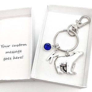 May include: A silver polar bear keyring with a blue gem, a silver letter K charm, and a silver key ring. The keyring is in a white gift box.