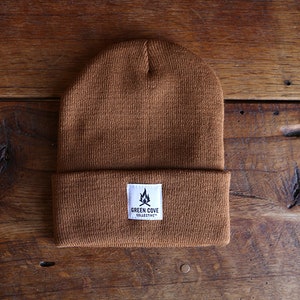 May include: A brown knit beanie with a white patch that says "Green Cove Collective" and a small campfire graphic.