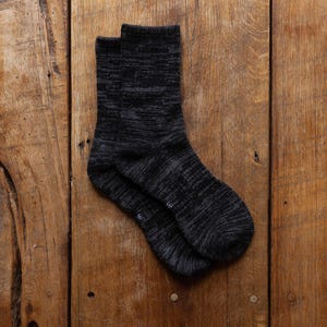 May include: A pair of dark gray socks with a speckled pattern. The socks are made of a soft, textured material and are folded neatly on a wooden surface. The socks are a neutral color and suitable for everyday wear.