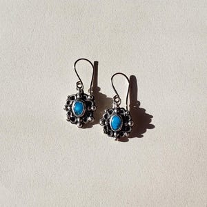 May include: A pair of silver dangle earrings with a turquoise stone set in a decorative silver frame.
