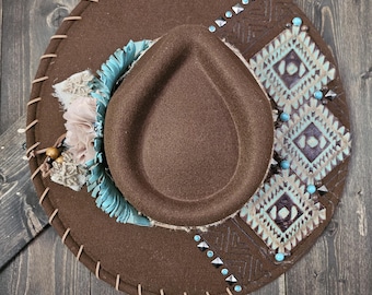 May include: A brown felt cowboy hat with turquoise and brown geometric designs, beaded accents, and a brown leather band.