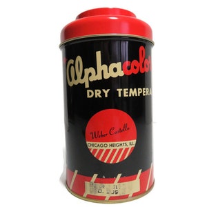 May include: A vintage tin container for Alphacolor Dry Tempera paint. The tin is black with red and gold lettering and a red lid. The label reads "Alphacolor Dry Tempera" and "Weber Costello, Chicago Heights, Ill."