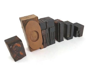 May include: A collection of vintage wooden letterpress printing blocks. The blocks are various sizes and shapes, with the letters "Q", "U", and "E" visible. The blocks are made of wood and metal, and are arranged on a white surface.