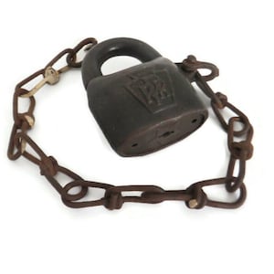 Könnte beinhalten: Ein antikes, dunkelbraunes Vorhängeschloss mit passender Kette und Schlüssel. Das Schloss hat ein geprägtes Design auf der Vorderseite. Kette und Schloss weisen Alters- und Abnutzungserscheinungen auf, was darauf hindeutet, dass es sich um Vintage-Artikel handelt. Der Schlüssel ist an der Kette befestigt.