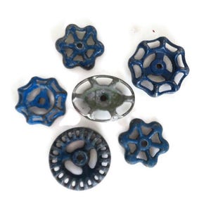 Peut inclure: Un assortiment de poignées de robinet vintage en métal bleu et argenté. Les poignées présentent divers motifs en étoile et circulaires. Le fond est blanc uni.
