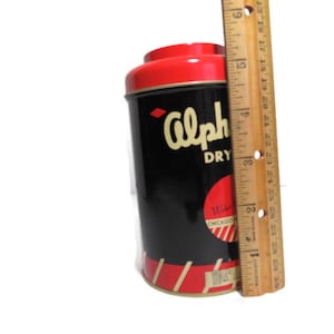 May include: A vintage tin can with a red lid and black body. The can has the text "Alpha Dry" and "Chicago, Ill." printed on it. The can is about 4 inches tall.