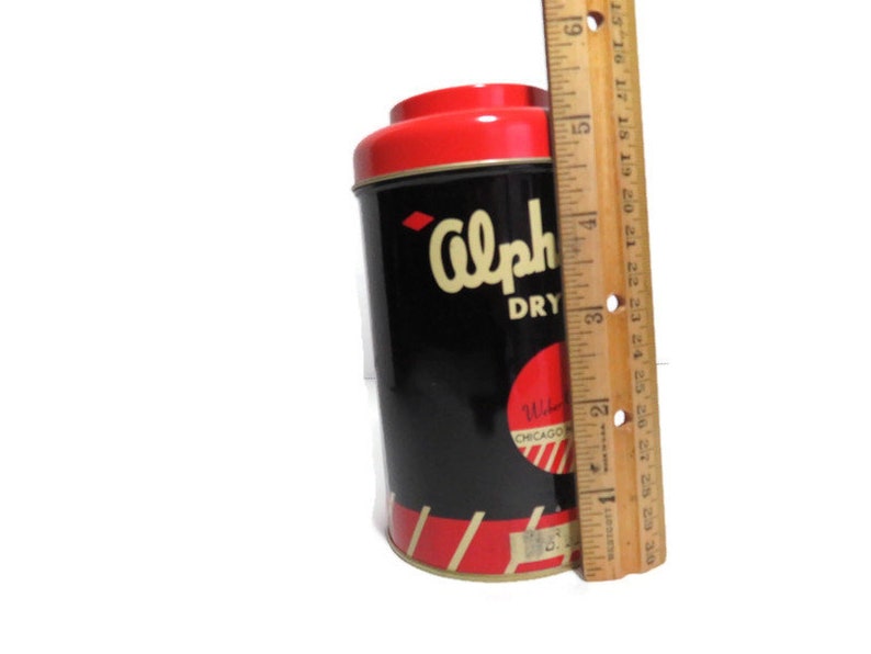 May include: A vintage tin can with a red lid and black body. The can has the text "Alpha Dry" and "Chicago, Ill." printed on it. The can is about 4 inches tall.