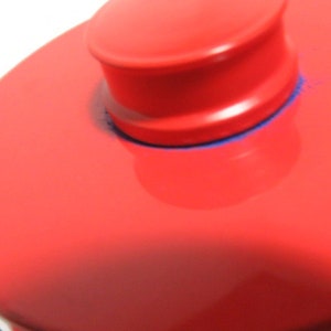 May include: A red, round, ceramic lid with a smaller, round, red knob on top. The knob has a blue rim.