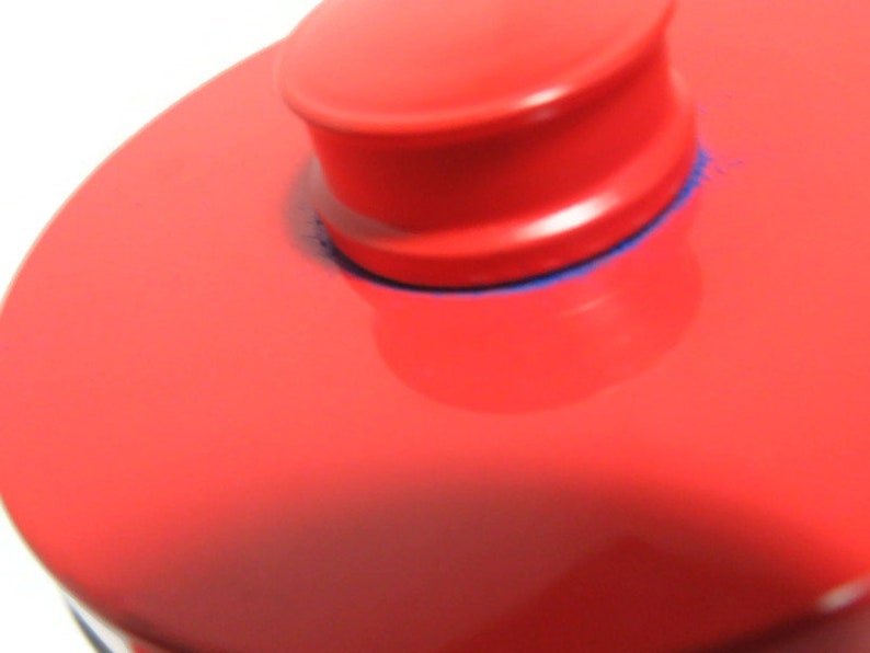 May include: A red, round, ceramic lid with a smaller, round, red knob on top. The knob has a blue rim.