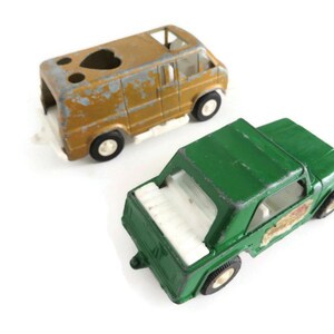 May include: Two vintage toy vehicles, a green jeep and a gold van. The jeep has a white interior and a white roof. The van has a white roof and a heart-shaped cutout in the roof.