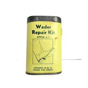 May include: A yellow metal tin with a black lid. The tin has a green and black illustration of a boot and the text "Wader Repair Kit Style A-1" and "CONTENTS: 30 SQ. IN. RUBBER TUBE CEMENT".