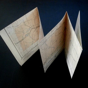 May include: A folded map with a detailed grid pattern and lines. The map is printed on cream-colored paper and has a light brown border.