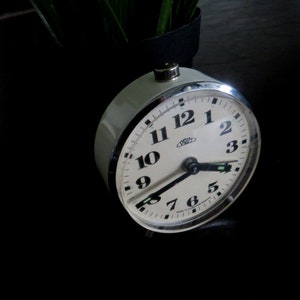 May include: A white analog alarm clock with black numbers and hands. The clock face reads "Primus" and has a black second hand.