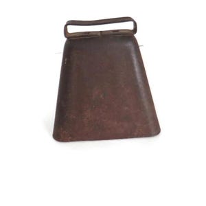 May include: A rusty brown metal cowbell with a handle.