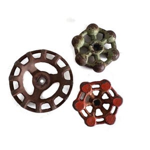 May include: Three vintage metal valve handles in varying shapes and colors. One is a rusty brown wheel, another is a green six-pointed star, and the third is a red six-pointed star. All have a distressed, aged appearance.