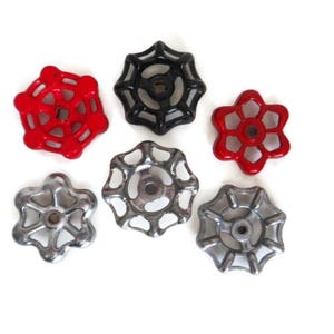 May include: A collection of six vintage valve handles in various colors and finishes. The handles include two red, one black, and three silver-toned metal pieces. Each handle has a unique, star-like design with multiple spokes.