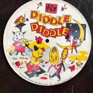 May include: Vintage Playsong record featuring the nursery rhyme "Hey Diddle Diddle." The circular record has colorful illustrations of a cat playing a violin, a dog, and other characters. The text "Hey Diddle Diddle" is prominently displayed in red and yellow.