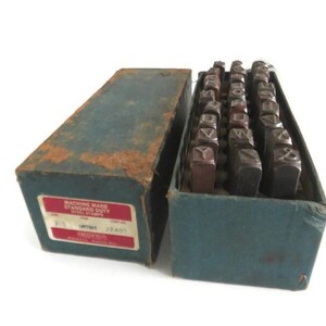 May include: A vintage blue box containing a set of metal letter stamps. The box is labelled "Machine Made Standard Duty Steel Stamps" and "Griffin 32.50".