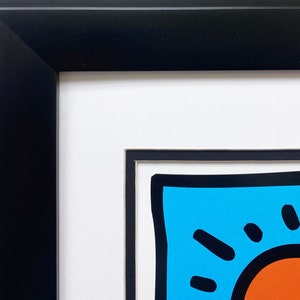 Puede incluir: Primer plano de una obra de arte enmarcada que presenta un dise&ntilde;o abstracto colorido con un fondo azul, un contorno negro y un c&iacute;rculo rojo en el centro.