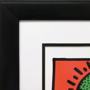 Puede incluir: Primer plano de una impresi&oacute;n enmarcada con un marco negro y un passe-partout blanco. La impresi&oacute;n presenta un fondo rojo con un dise&ntilde;o de sol negro y verde.