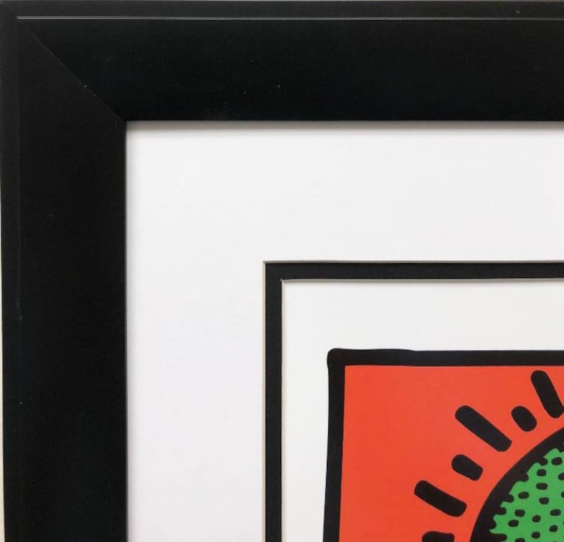 Puede incluir: Primer plano de una impresi&oacute;n enmarcada con un marco negro y un passe-partout blanco. La impresi&oacute;n presenta un fondo rojo con un dise&ntilde;o de sol negro y verde.