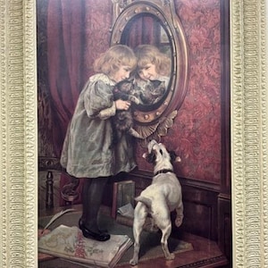 May include: A framed vintage print depicts a young girl in a dress holding a cat in front of a mirror. A small dog stands on its hind legs, looking up at the cat. The artwork is set against a backdrop of red floral wallpaper and a dark red curtain.