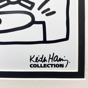 K&ouml;nnte beinhalten: Schwarz-wei&szlig;e Linienzeichnung einer Figur mit einer Unterschrift, die "Keith Haring COLLECTION" lautet.
