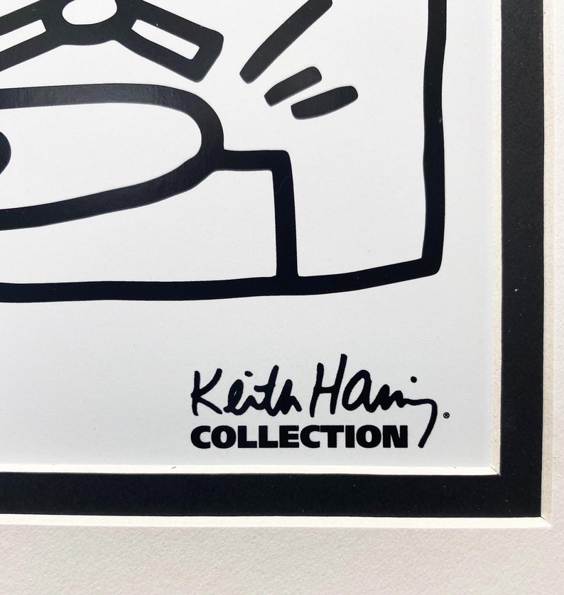 K&ouml;nnte beinhalten: Schwarz-wei&szlig;e Linienzeichnung einer Figur mit einer Unterschrift, die "Keith Haring COLLECTION" lautet.