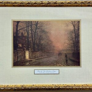 May include: Framed print of a landscape scene with a road, trees, and a building. The print is in a gold ornate frame. The scene depicts a person walking on a road with a horse-drawn carriage in the distance. The print has a soft, muted color palette.