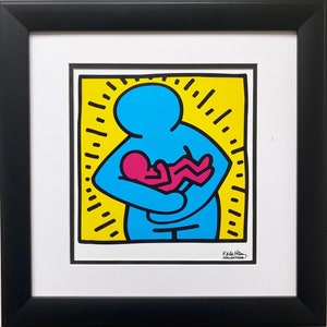 May include: A framed print of a colorful illustration of a blue figure holding a pink figure. The background is yellow with black lines. The print is signed "Keith Haring Collection".