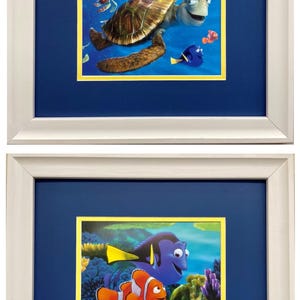 May include: Two framed pictures of characters from the animated movie Finding Nemo. The top picture shows a green sea turtle swimming with other fish. The bottom picture shows a blue tang fish and an orange clownfish swimming in a coral reef.