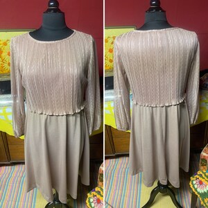 May include: A long-sleeved dress with a pleated bodice and a solid skirt. The dress is a light brown color and has a vintage style.