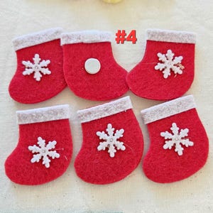 Könnte beinhalten: Sechs kleine, rote Weihnachtsstrümpfe aus Filz mit weißen Schneeflockenapplikationen und weißem Besatz. Ein Strumpf hat einen weißen Kreis angebracht. Die Nummer "#4" ist im Bild zu sehen.