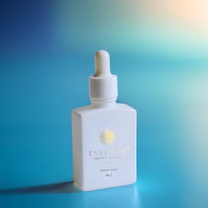May include: A white square bottle with a dropper top. The bottle has gold text that reads "ESSENCE 64 EMBODY DIVINE SIDDHC DROPS". The background is a gradient of blue and teal.