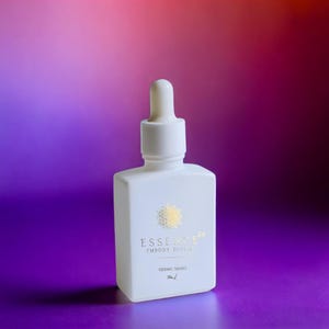 May include: A white, square-shaped bottle with a dropper top. The bottle has gold text that reads "ESSENCE" and "EMBODY DIVINE". The bottom of the bottle reads "SIDERIC DROPS" and "5ml". The background is a gradient of purple, red, and orange.