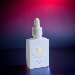 May include: A white square bottle with a dropper top. The bottle has gold text that reads "ESSENCE EMBODY DIVINE" and "SIDERIC DROPS". The background is a gradient of red, purple, and blue.