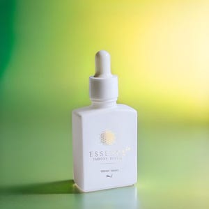 May include: A white square bottle with a dropper top, featuring gold text and a decorative emblem. The bottle is labeled "ESSENCE EMBODY DIVINE" and "SIDERIC DROPS". The background is a gradient of green and yellow.